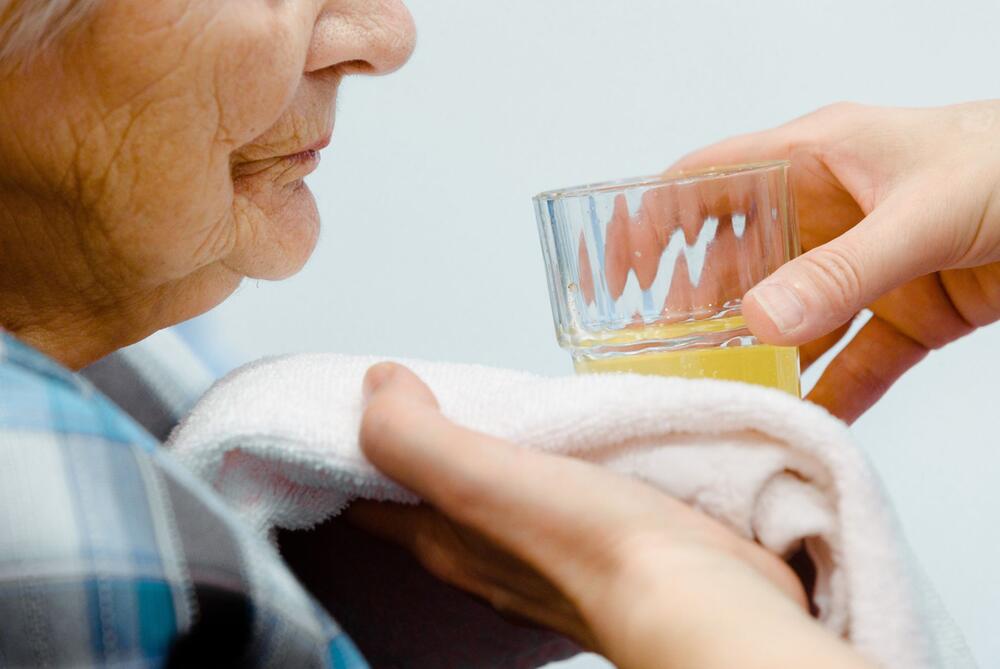 Pfleger reicht einer Bewohnerin eines Altenheims ein Glas Wasser
