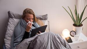 Eine Frau liegt krank im Bett und guckt auf ihren Tablet-Computer