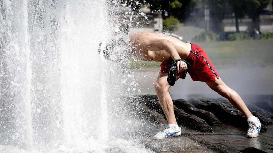 Ein Passant erfrischt sich bei großer Hitze am Brunnen