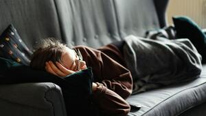 Eine Person mit Brille liegt auf einer grauen Couch, stützt den Kopf auf ein dunkles Kissen und ...