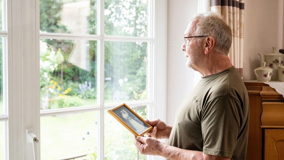 Mann steht mit einem Hochzeitsfoto am Fenster