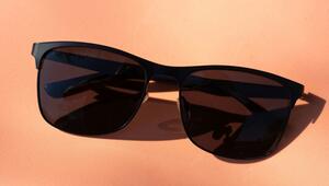 Schwarze Sonnenbrille mit dunklen Gläsern auf einem hellorangefarbenen Untergrund.