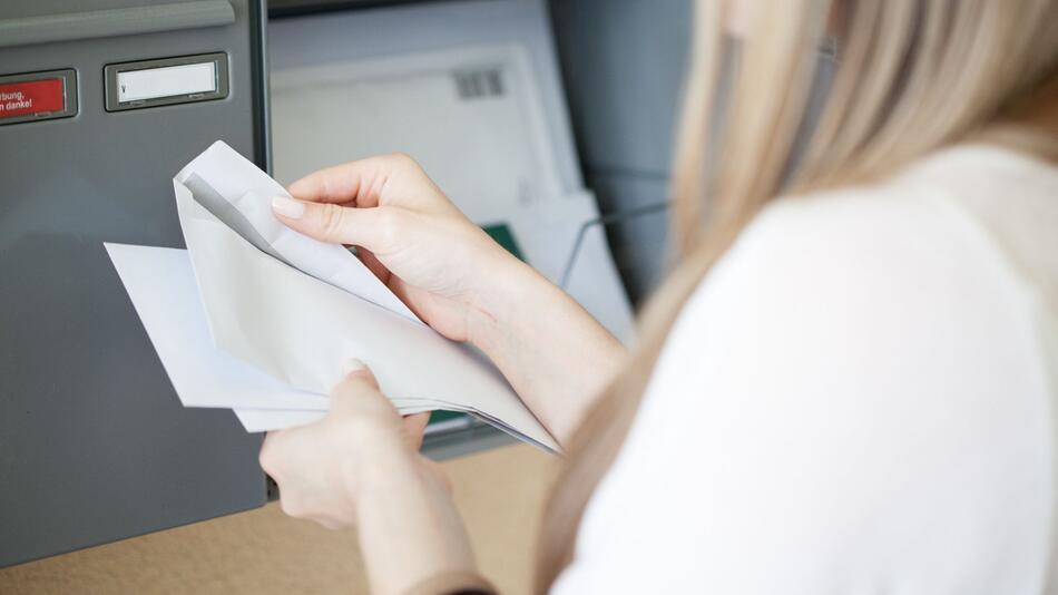 Eine Frau holt Post aus dem Briefkasten