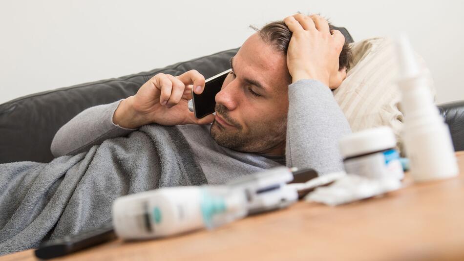 Mann liegt krank auf einem Sofa und telefoniert