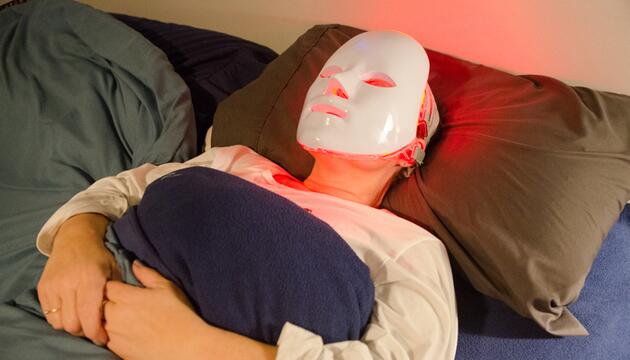 Frau zu Hause mit LED-Maske im Bett