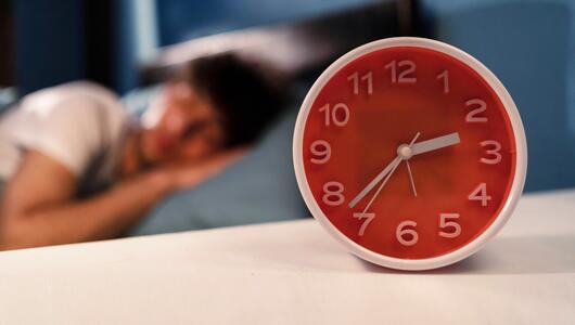 Mensch liegt im Bett, davor ein Wecker, dessen Uhrzeit auf 2:37 Uhr steht