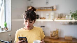 Frau steht in der Küche und blickt aufs Handy 