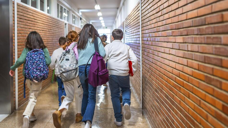 Schüler, die mit ihren Taschen durch den Flur einer Schule laufen.