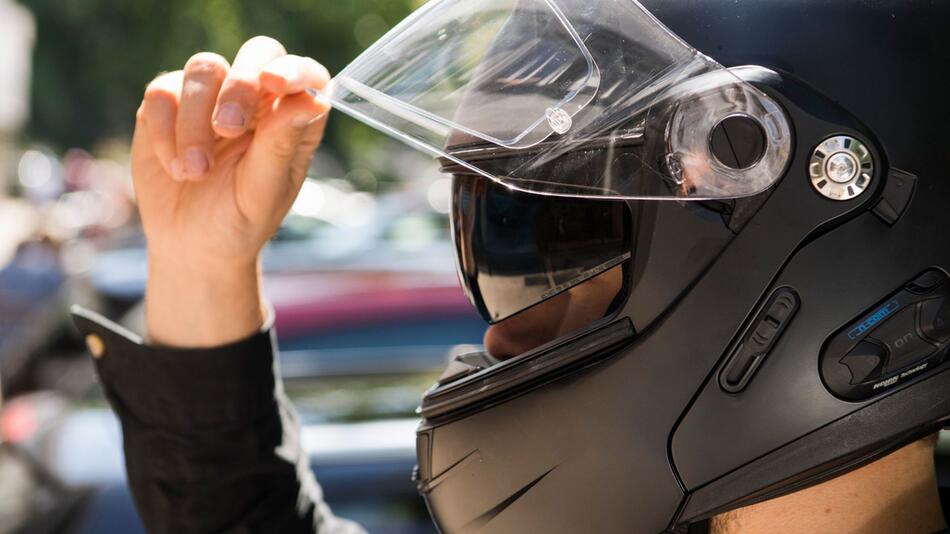 Ein Motorradfahrer hebt das Visier seines Helms an