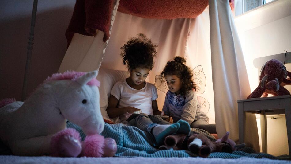 Zwei Kinder sitzen in einem Zelt im Kinderzimmer und lesen