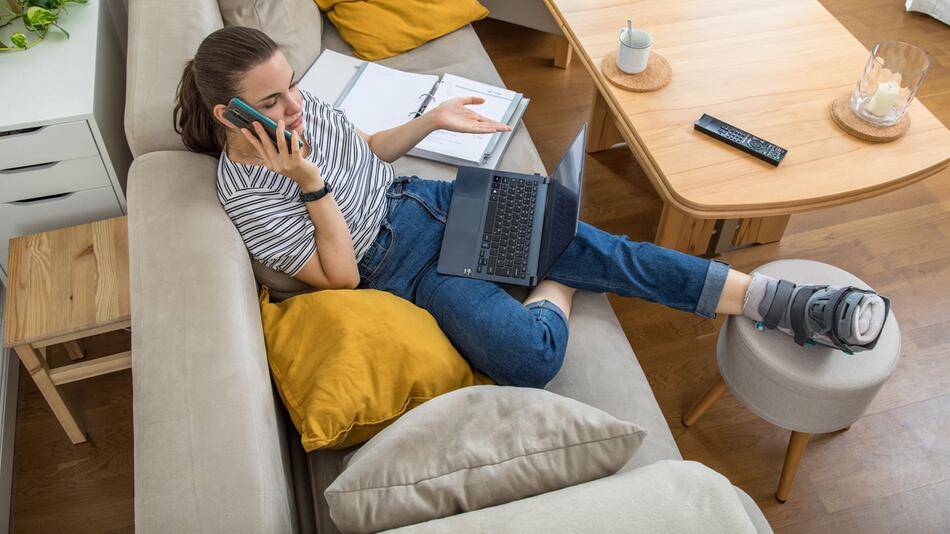 Eine Frau mit gebrochenen Fuß telefoniert auf dem Sofa