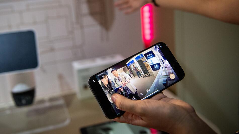 Eine Frau steuert mit einem Smartphone eine Ueberwachungskamera
