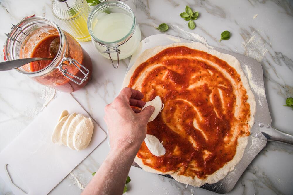 Eine Frau belegt Pizza mit Mozzarella