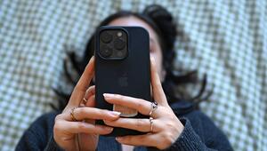 Eine junge Frau liegt mit dem Smartphone in der Hand auf dem Bett