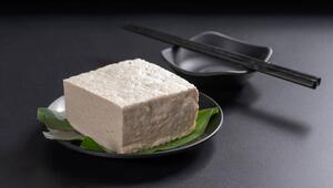 Ein Tofublock liegt auf einem schwarzen Teller. Daneben liegen Stäbchen.