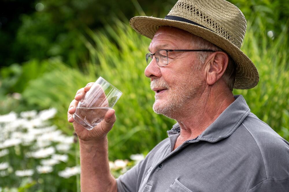 Ein Senior trinkt ein Glas Wasser im Sommer
